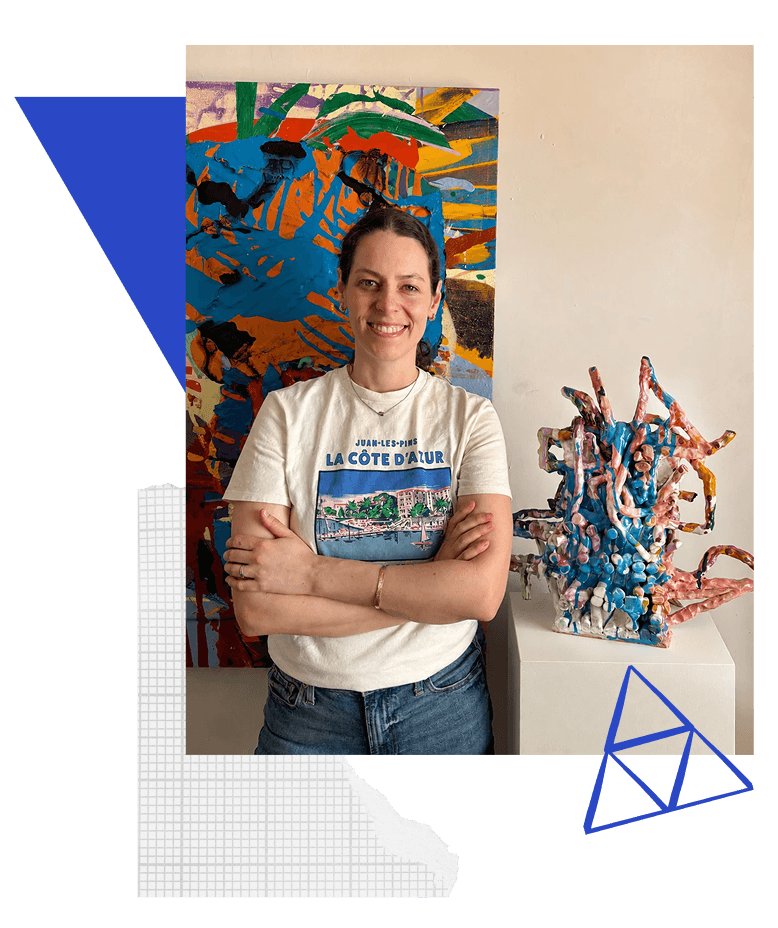 Katie Kirk in her studio, standing between one of her paintings and a glazed ceramic sculpture.
