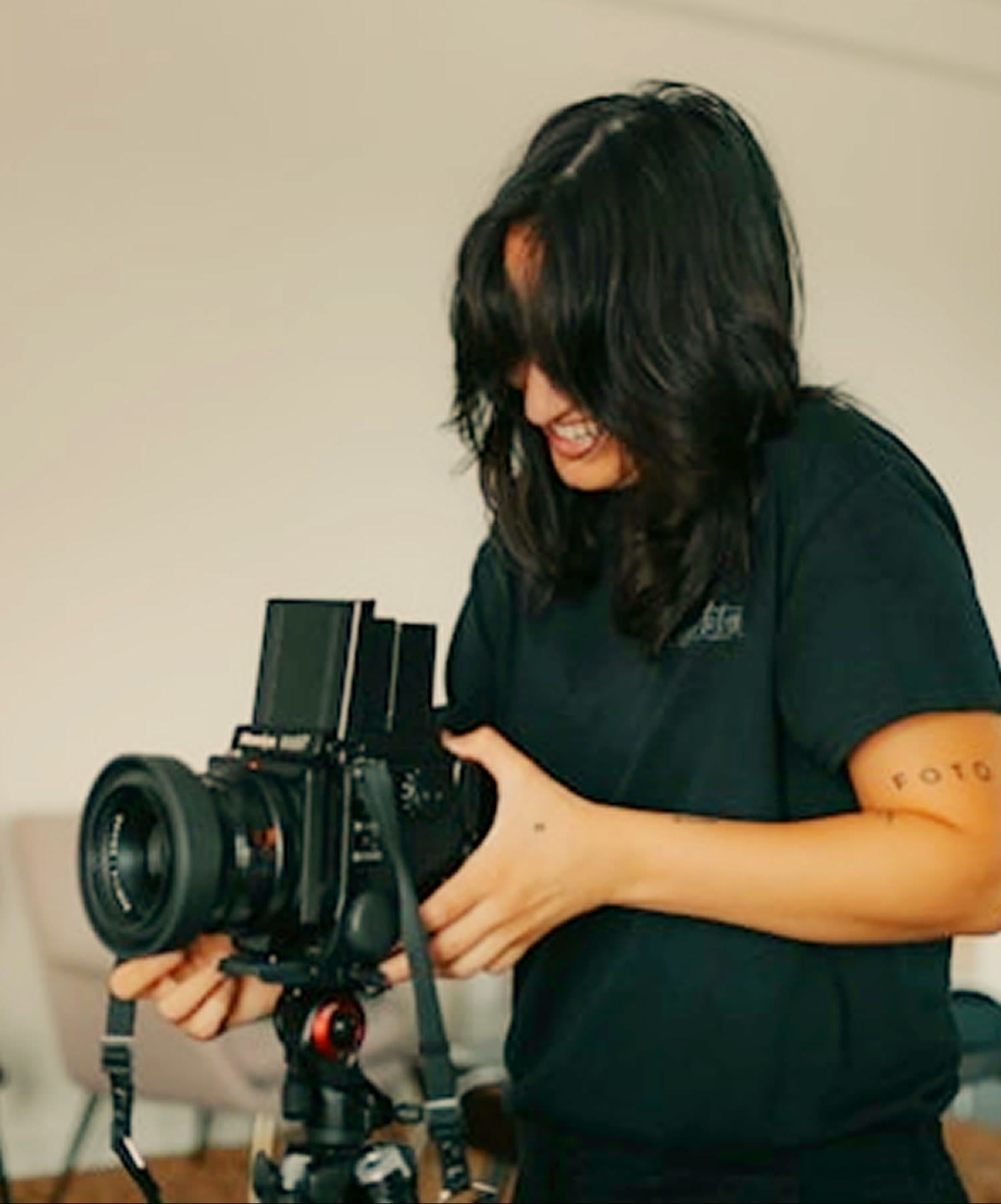 A photographer adjusting a medium-format camera on a tripod in a daylit studio.